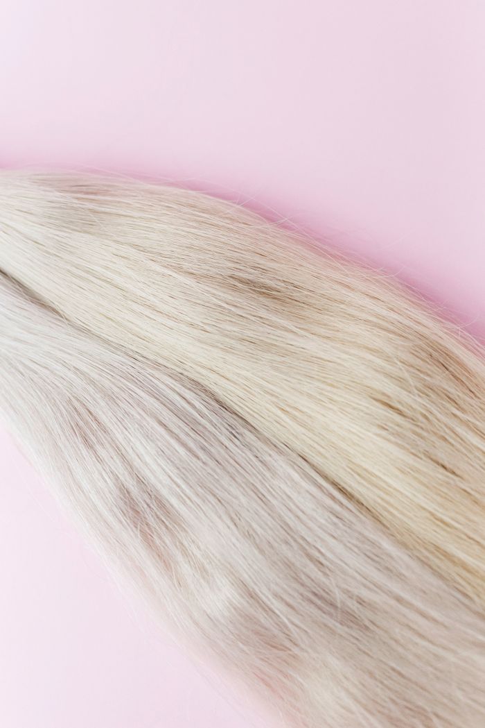 Close-up of blond hair on a pastel backdrop, showing texture and color.
