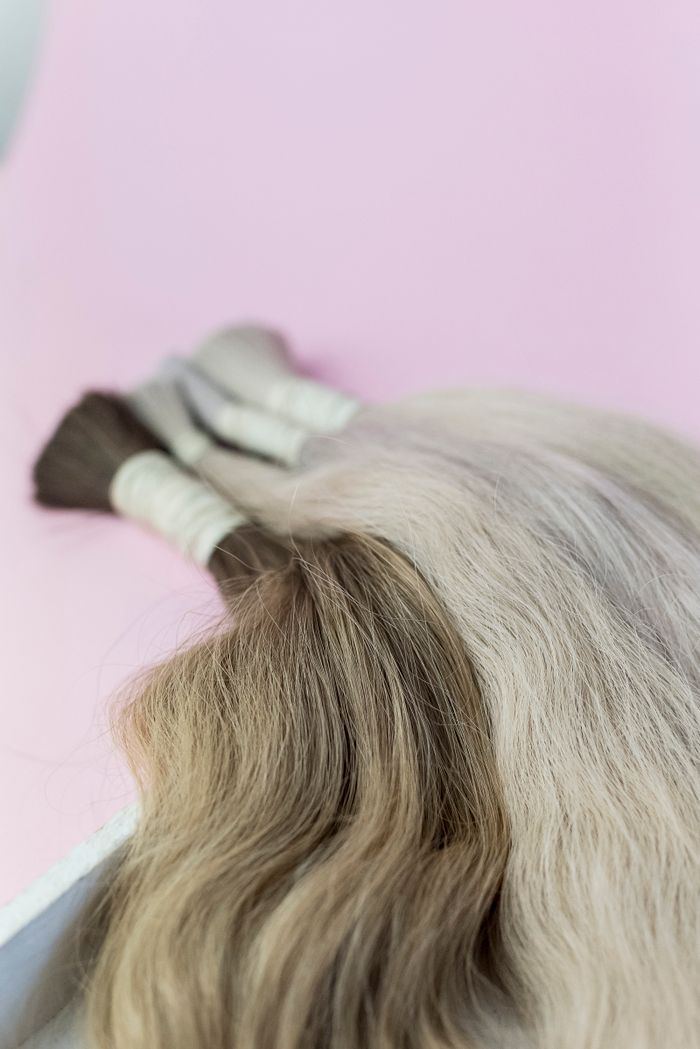Close-up of blonde hair extensions against a light pink background.